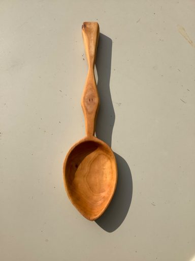 Wooden spoon with a smooth, rounded bowl and a slender handle, resting on a light surface.