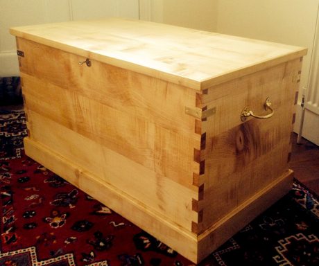 Wooden chest with a smooth finish and decorative wooden joints, placed on a patterned rug.