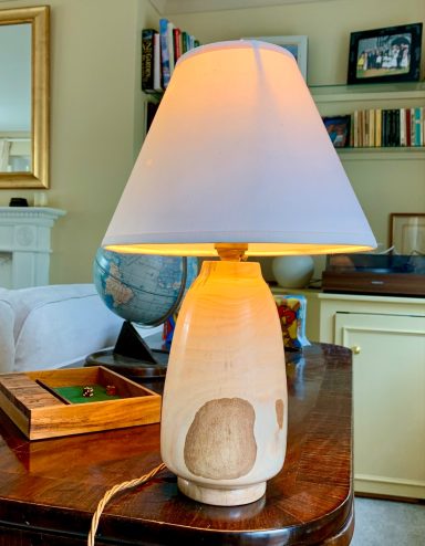 A wooden lamp with a white shade, glowing warmly, placed on a wooden table.