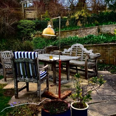 Garden seating area with wooden furniture and a lamp, surrounded by greenery.
