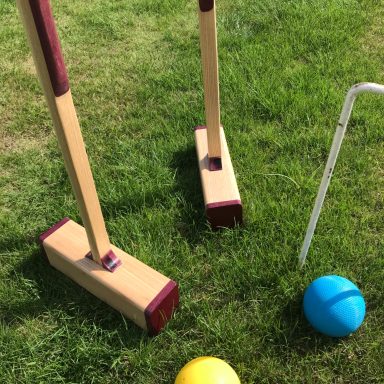 Croquet mallets and balls (yellow and blue) on grass.