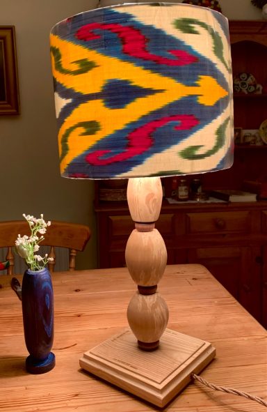 Decorative lamp with a patterned shade on a wooden base, next to a small vase.