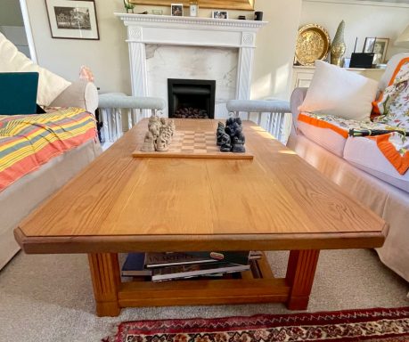 A wooden coffee table with chess pieces, surrounded by sofas and a fireplace.