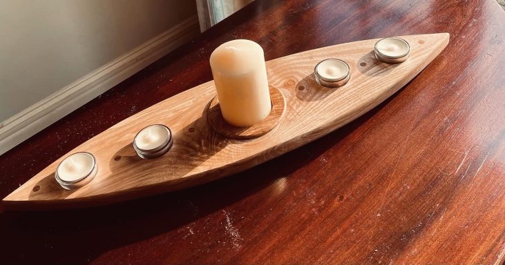 A wooden boat-shaped candle holder with a central pillar candle and three tea lights.